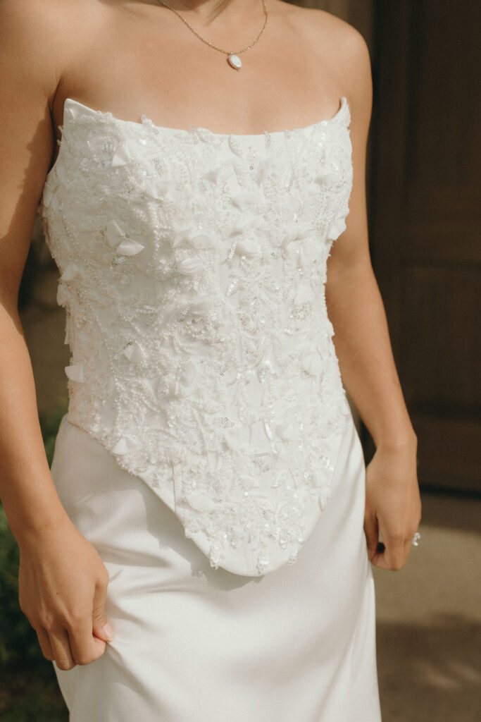 Close-up of Kiana’s hands and the intricate hand-beaded detailing on the bodice of the “Rayne” gown from Dalliance Gown Rentals, captured during her Monserate Winery engagement session.